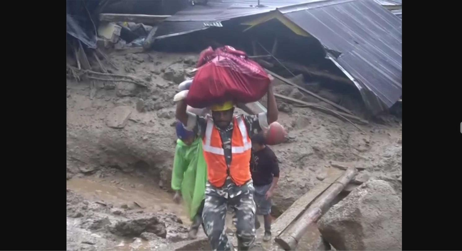 Relief worker carrying salvaged belongings through debris in Rimbi